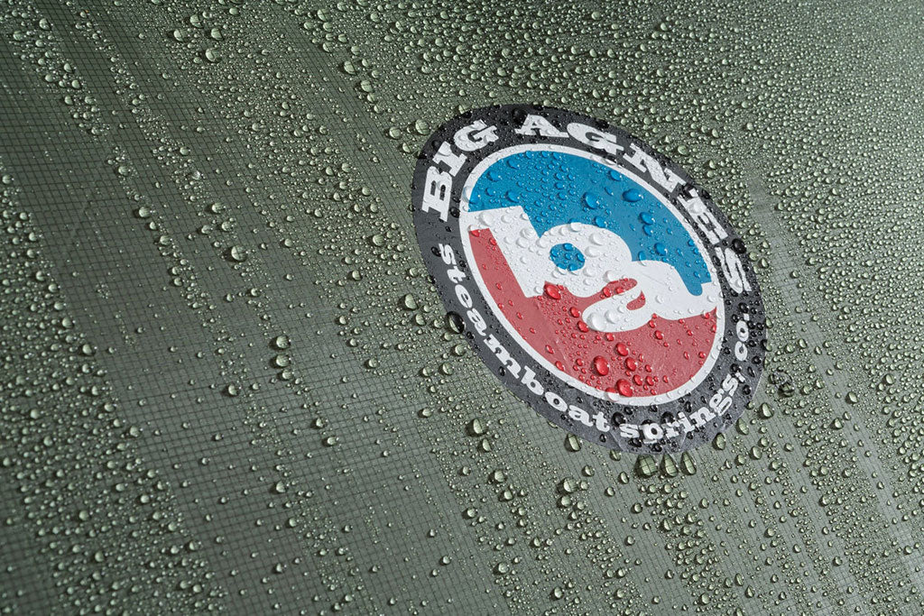 Big Agnes logo on wet green fabric with water droplets, showing water-resistant coating.