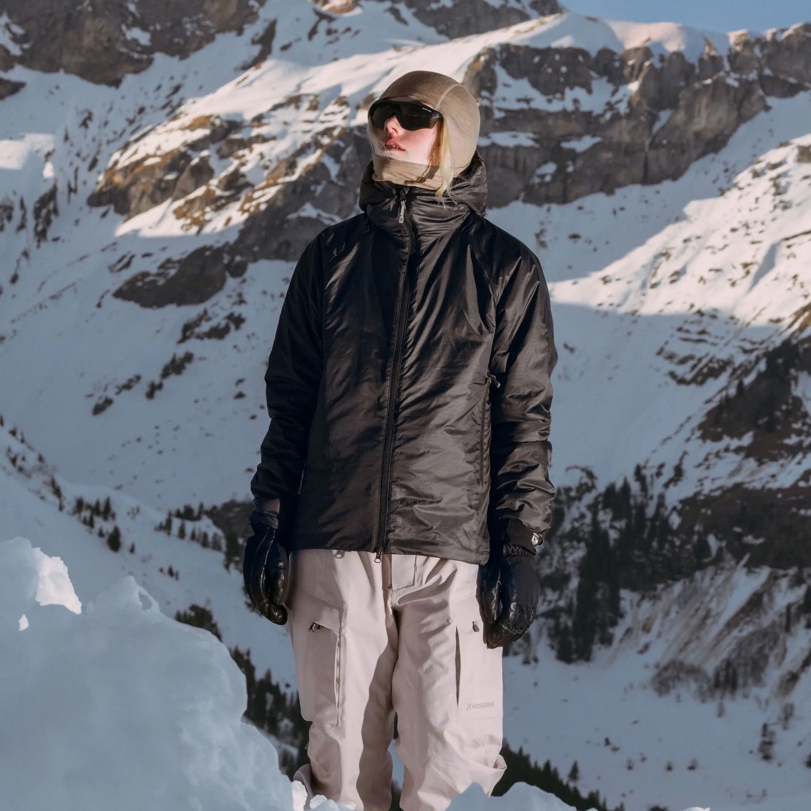 Houdini Dunfri jacket worn by a person in snowy mountains with sunglasses and a beige hood.