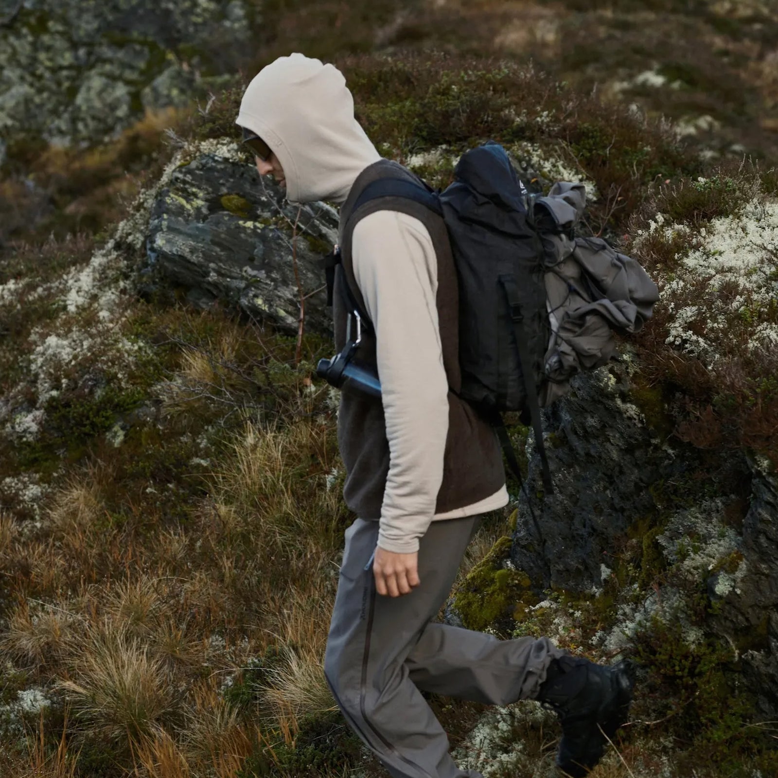A hiker wearing Houdini Lykan series gear navigating rocky, moss-covered mountain terrain.