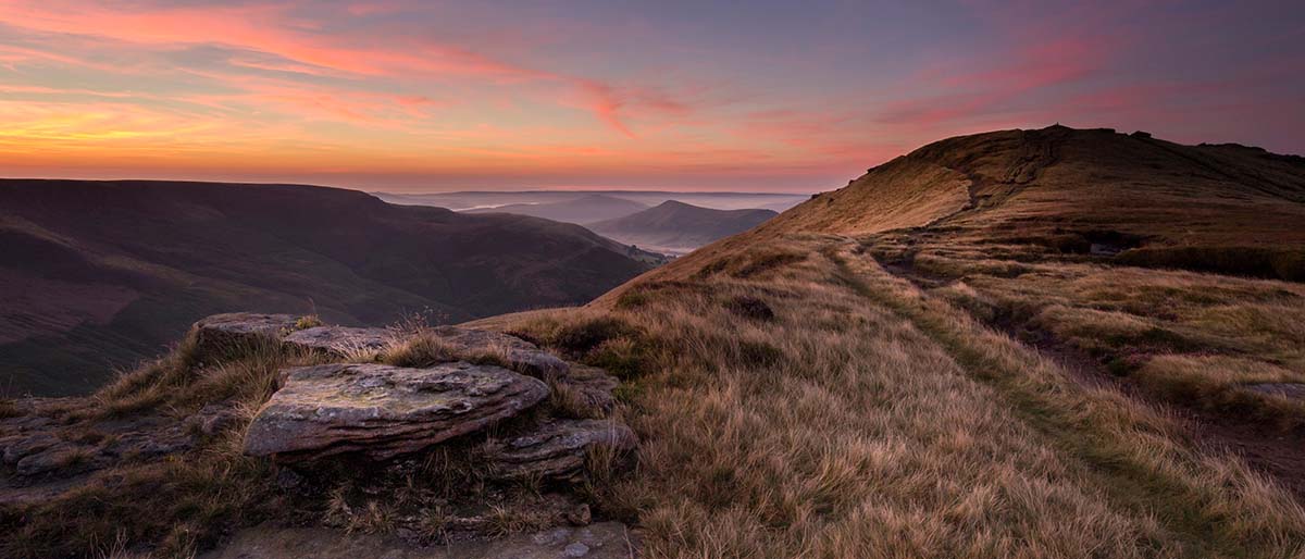 Sunrise over moorland ridge from Grindslow Knoll with layered hills in distance, Peak District