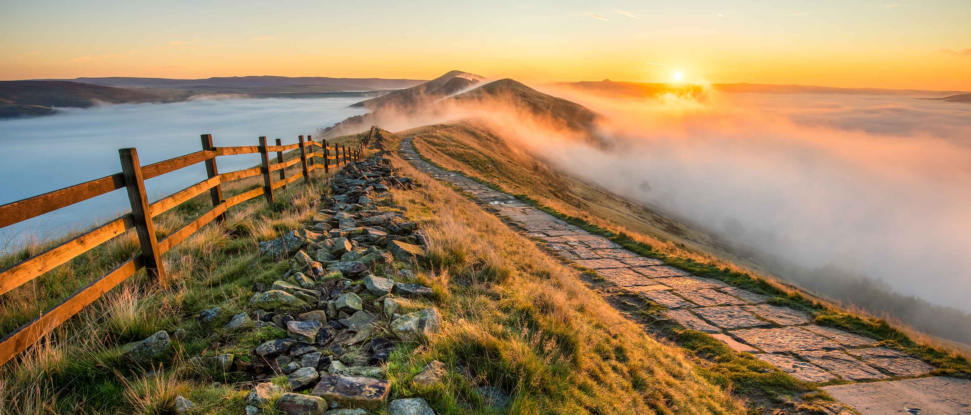 Thick cloud inversion with morning sun casting golden light on the landscape at Mam Tor in the Peak District.  