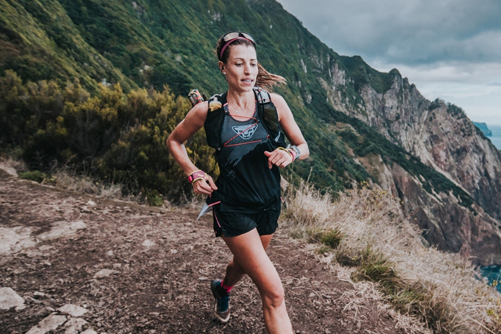 A runner in black gear with a backpack trail running on a mountainous coastal path during the Madeira Ultra Race.