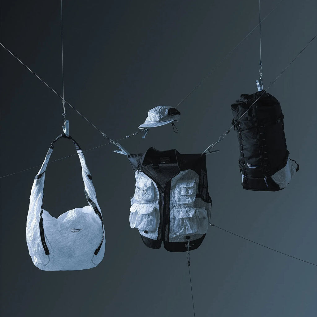 Outdoor gear including a white shoulder bag, reflective gilet, black backpack and cap suspended