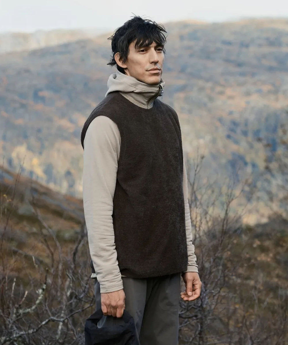 Houdini Lykan gilet worn over a long-sleeve base layer, modelled on a hillside with woodland views.