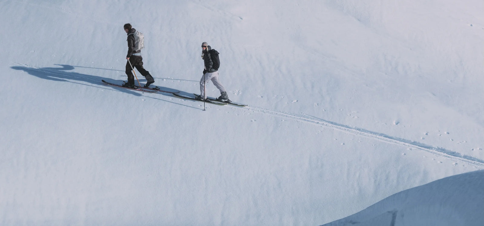 Two skiers traversing a snowy mountain slope in Houdini winter gear.
