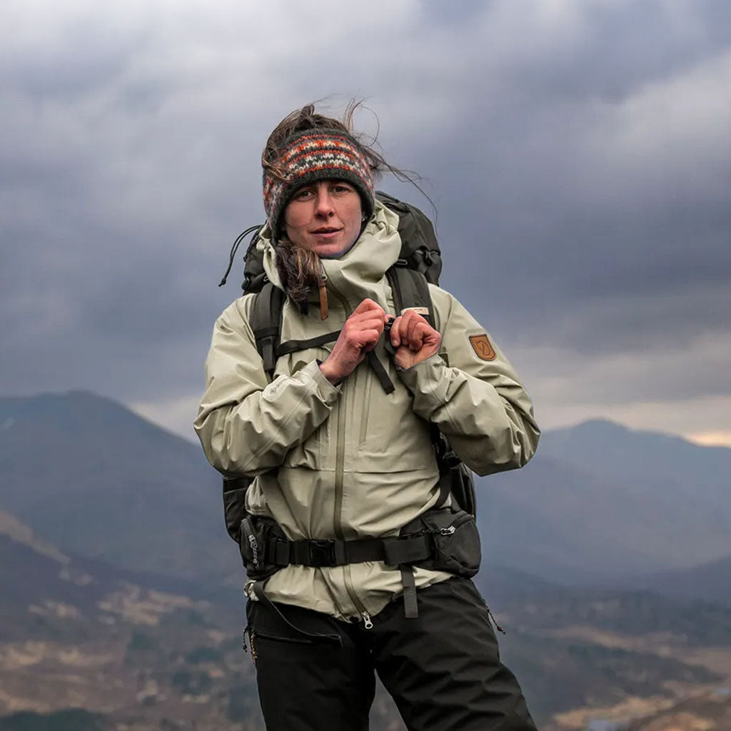 Woman hiker in Fjallraven jacket and knit beanie with rucksack, mountains in background