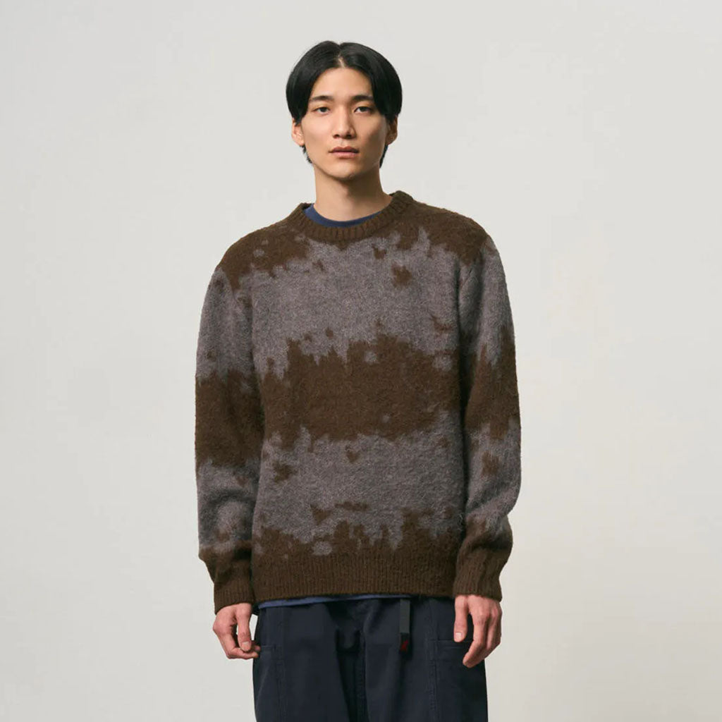 Man wearing Gramicci brown and grey striped knit crewneck sweater with navy trousers.