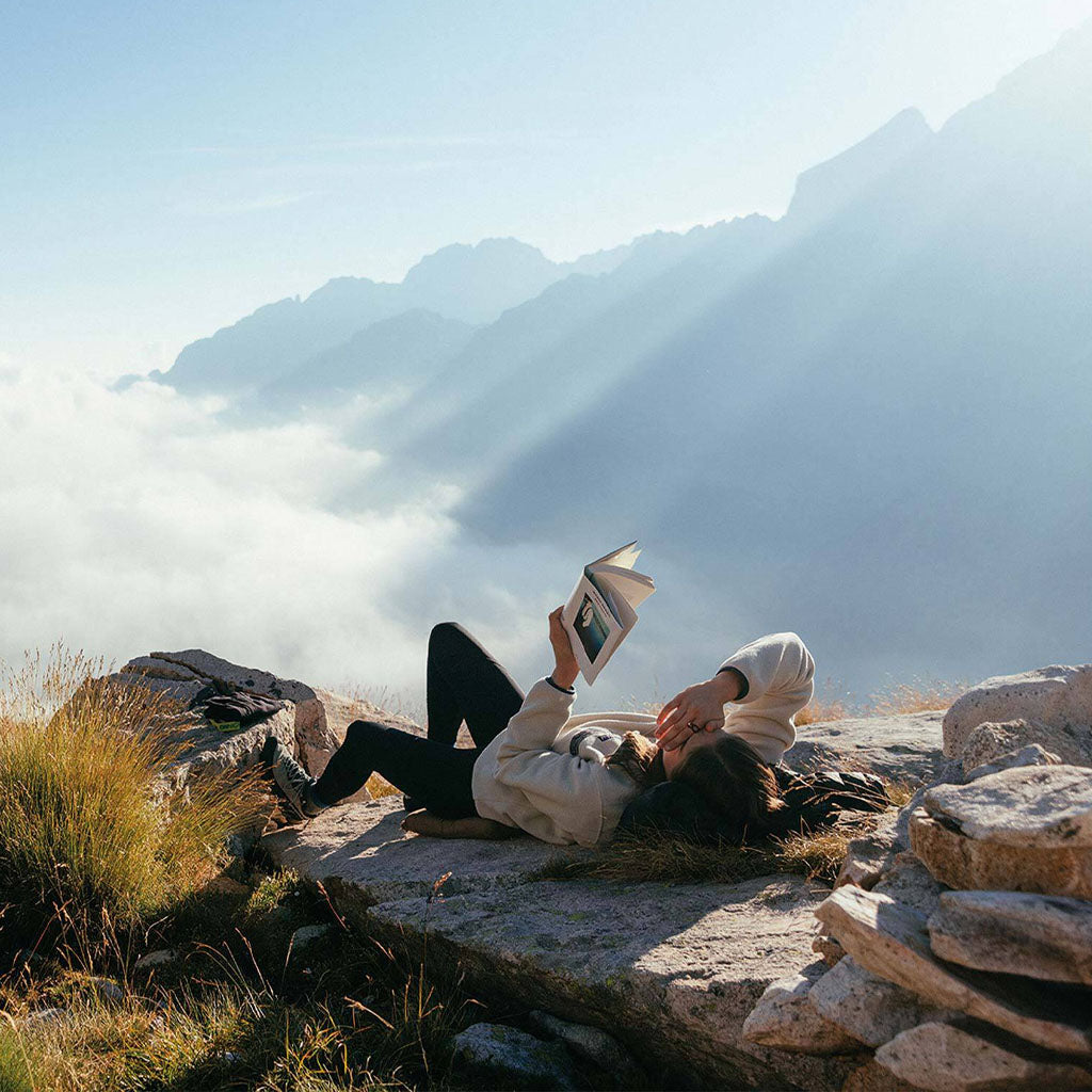 A hiker resting on a rocky mountain ridge with a map, overlooking misty valleys and peaks.