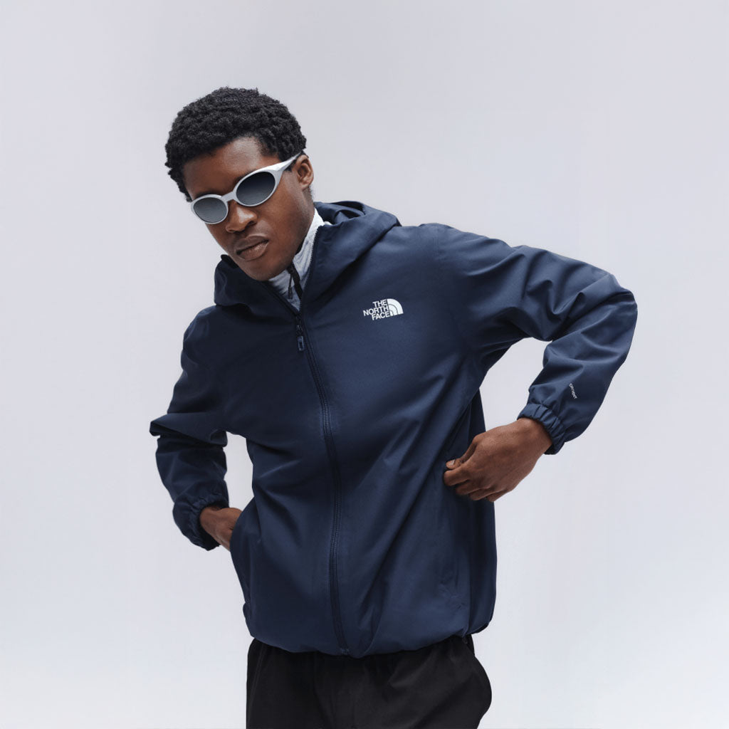Person wearing The North Face navy hooded jacket and white sunglasses against a light grey background.