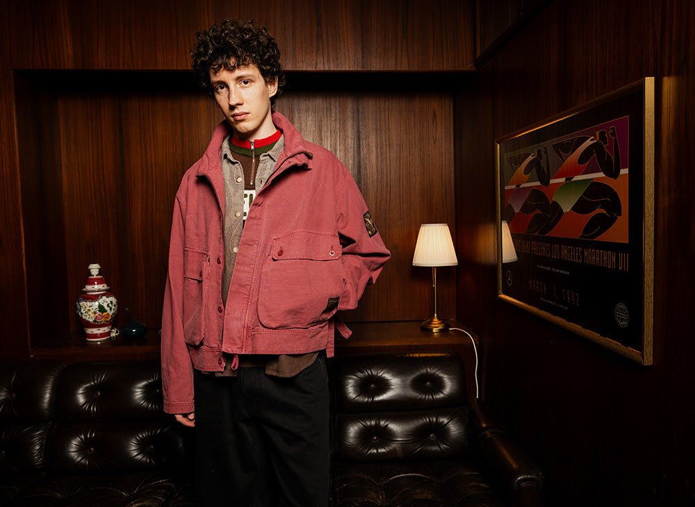 Person wearing a pink cotton jacket over layered tops in a wood-panelled interior setting.